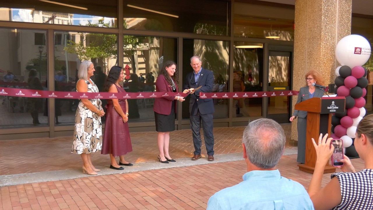 University representatives cut a garnet ribbon outside a campus building as a speaker addresses attendees during a ribbon-cutting ceremony.