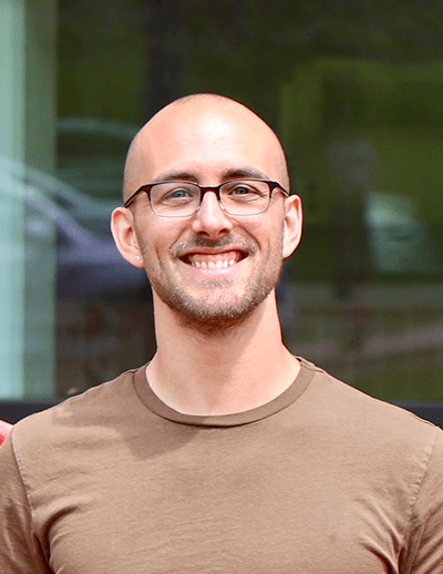 Sean Ehlman, incoming USC biology faculty member, smiling outdoors in a brown shirt and glasses.