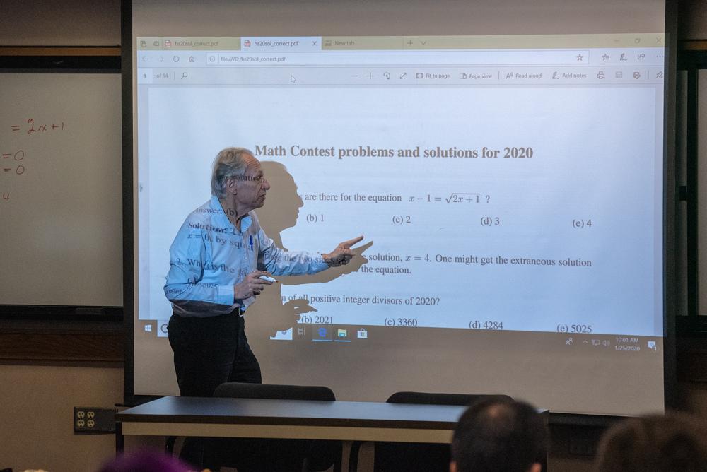 Professor going over a math problem projected on the screen behind him