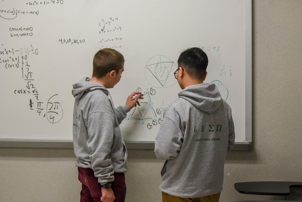 Students working a math problem at a whiteboard
