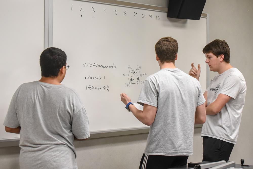 Students working a math problem at a whiteboard