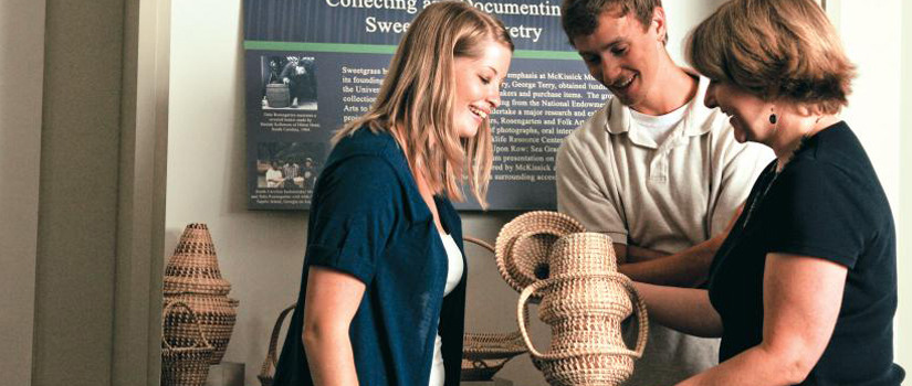 Curator engages two students with a sweetgrass basket. 
