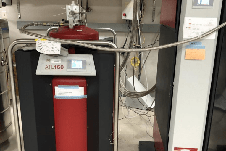 A red container on the left is connected to a system on the right via a pipe.