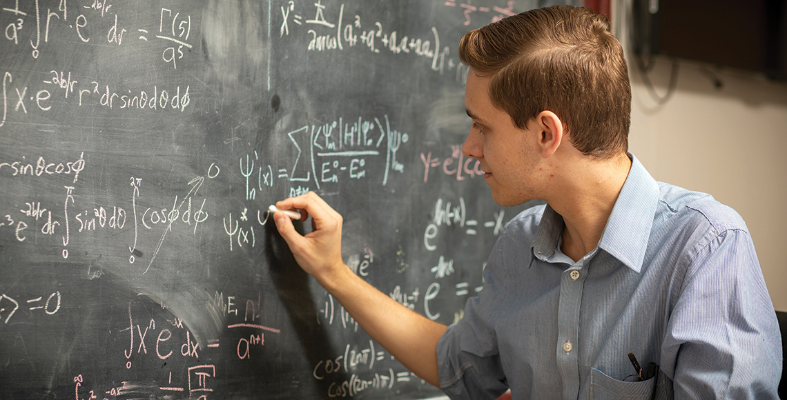 Eric Rohm (physics student) completing a complicated equation on a chalkboard