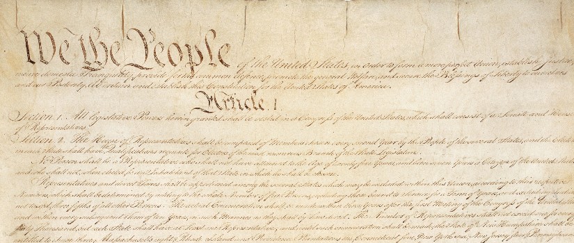 Image of the U.S. Constitution. Brown paper with writing on it. Legible phrases include "We the people" and "Article One" is legible