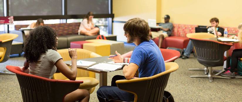 Two students talking while sitting on comfy chairs in Russell House