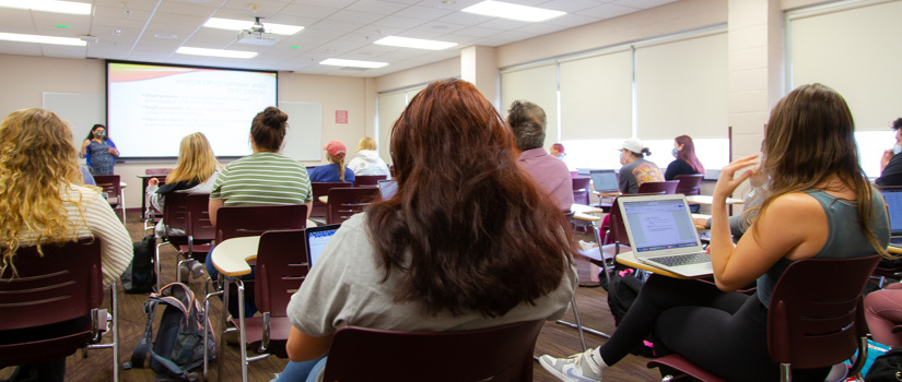 A dozen students sit in a classroom facing the instructor at the front of the class.