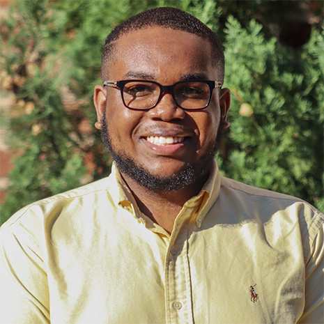 Psychology student Timothy Simmons smiles at the camera, he is wearing black framed glasses and a yellow dress shirt.
