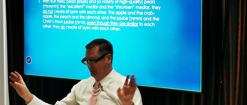 Professor giving a presentation in front of a screen displaying “Mishnah Kilayim 1:4” during a conference talk.
