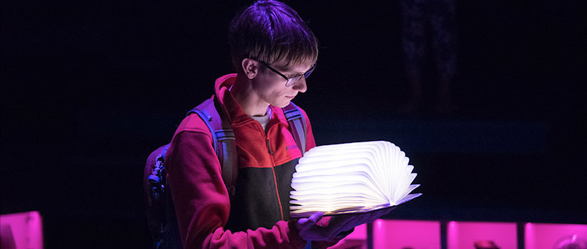 Actor on stage looking into lit up book