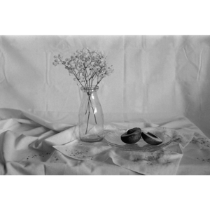 A black and white photo of flowers in a vase next to an opened fruit