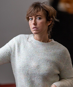 Person with short, tousled brown hair wearing a light-colored knit sweater, looking directly at the camera with a neutral expression.