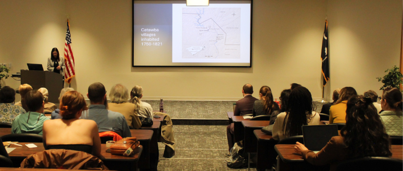 audience at the Waters Lecture looking at a map on a screen with the speaker in front