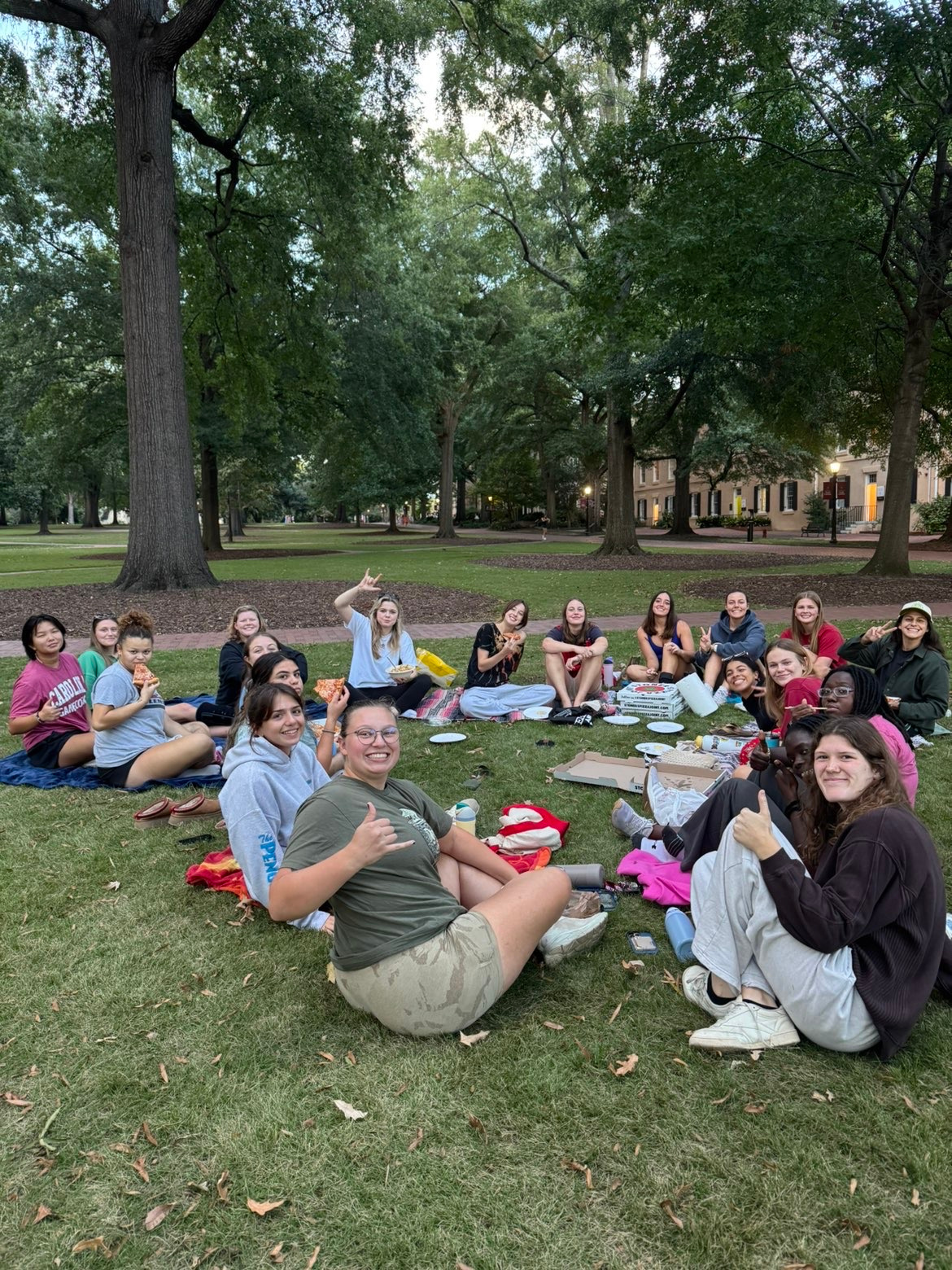 members of the team enjoy a team dinner seated outside on the Horseshoe on the Columbia campus. they smile at the camera and pose with their pizza