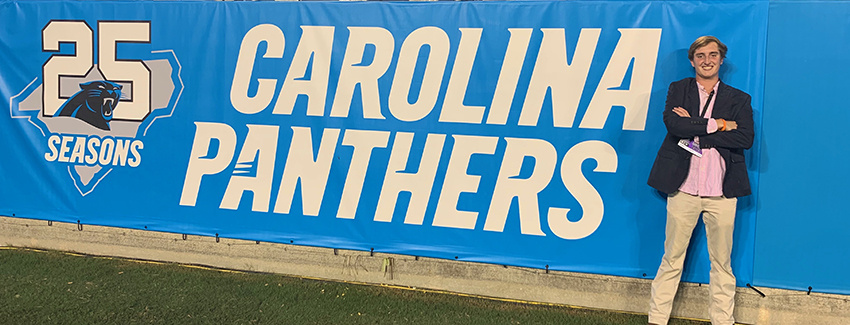 Alumnus Lee Wardlaw standing in front of a Carolina Panthers banner.