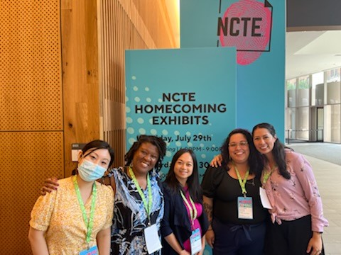 Five women of varied nationalities standing in front of a sign that reads "NCTE Homecoming Exhibits"