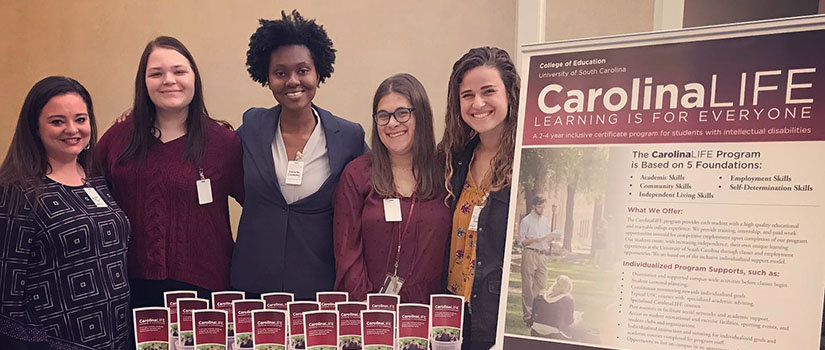 CarolinaLIFE participants smile at the camera amidst signs and pamphlets about the program.
