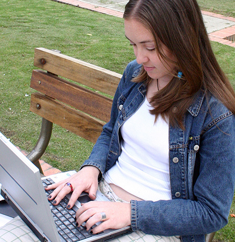 a white woman wearing a denim jacket working on a laptop on a public bench