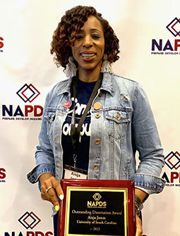 Aisja Jones standing in front of NAPDS tiled background holding a plaque