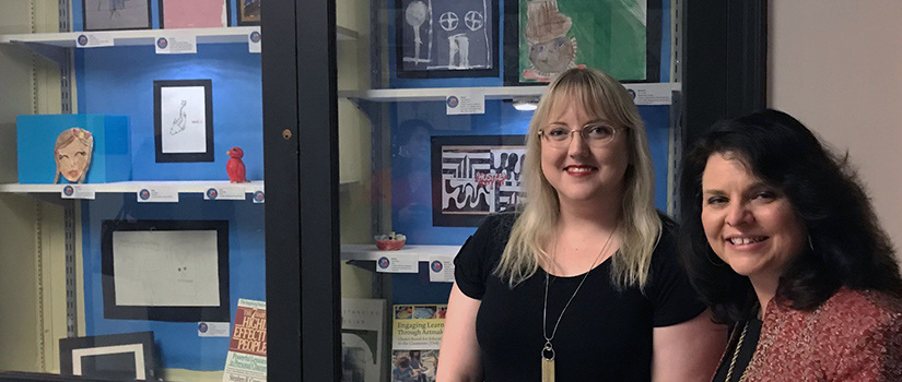 two women in front of a display of children's artwork