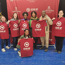 children and adults holding up red t-shirts with the words "GEAR UP SC" printed on them.