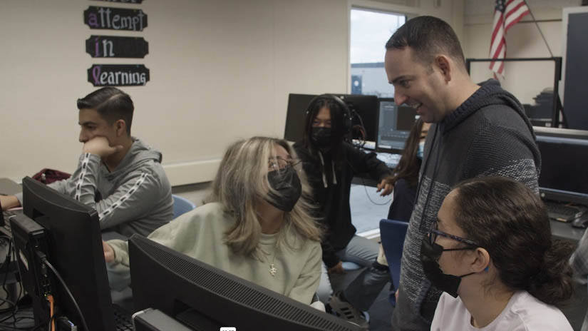 masked students in a classroom full of computers stalking with smiling teacher