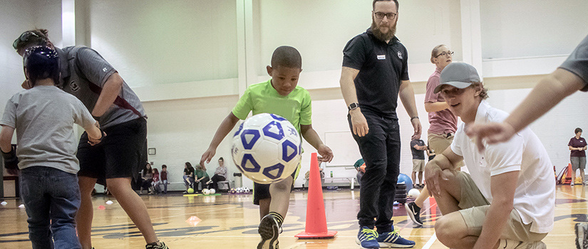 An adapted physical education teacher leads a student in a physical activity involving a soccer ball