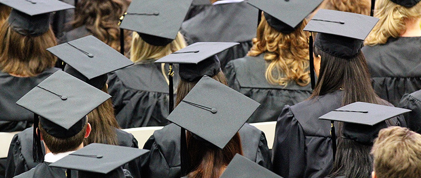 several people in black graduation caps and gowns, seen from behind.
