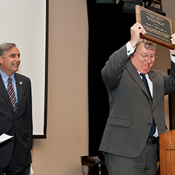 Bud Ferrillo holds the Travelstead award while former UofSC President Harris Pastides looks on.