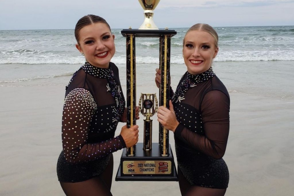 2 Dance team members holding a trophy on the beach