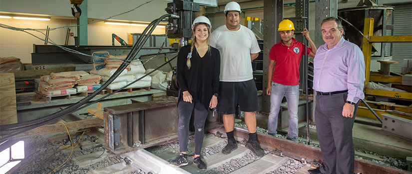 three grad students stand in the railway lab with Rd. Rizos