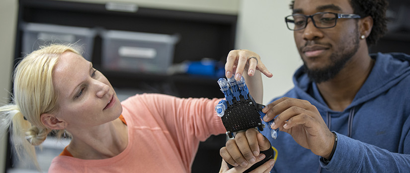 a faculty member fits a student with a robotic arm