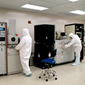Two people in white personal protective gear working in a lab, shows researchers working inside a microelectronics cleanroom facility.
