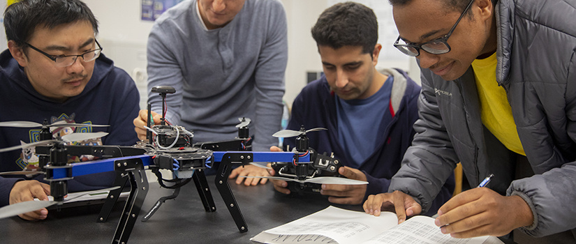 four male students sit at a table and work on drone