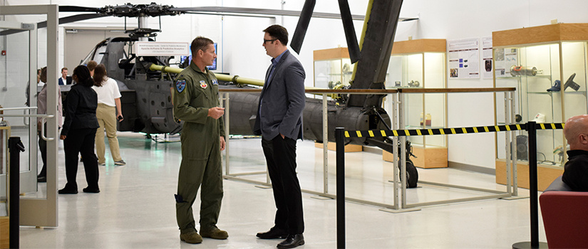 Two men stand in front of a helicopter in the McNair Center.