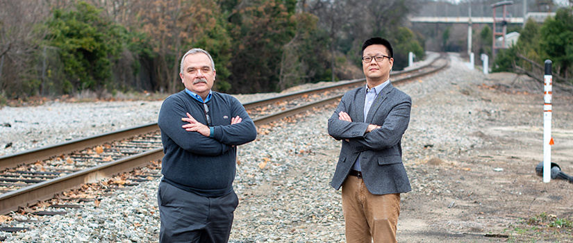 Rizos and Qian stand next to a railroad track.