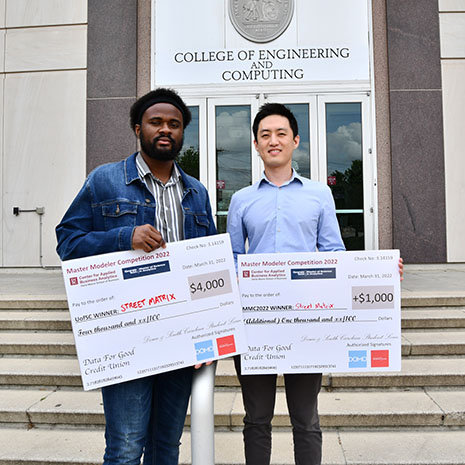 Two men holding two large checks