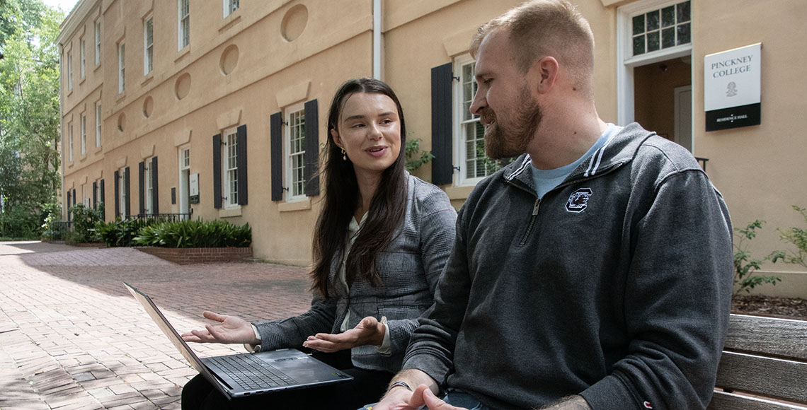 Young woman with a computer talks with a professor.
