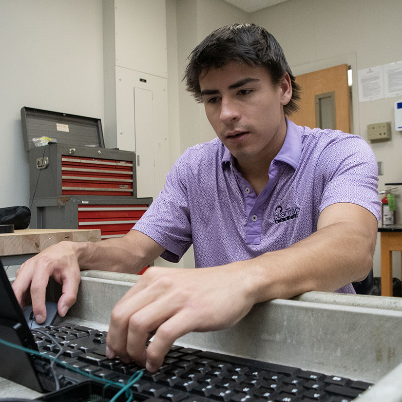 Kam Davis typing on a laptop in an electrical engineering lab. 