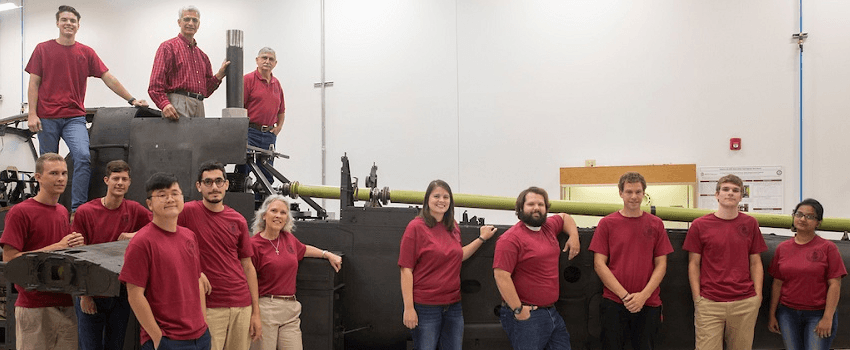 research team poses in front of apache helicopter in Mcnair Center