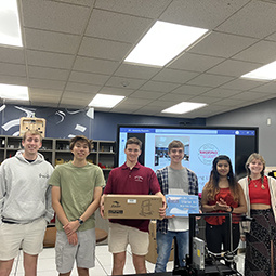 Group of students in the makerspace. Two are holding boxes.