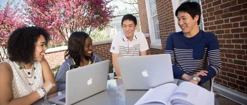 four students at table with two laptops on top of the table