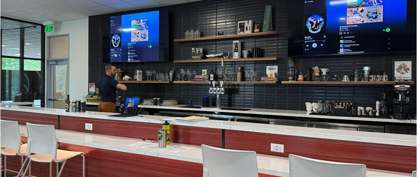 Man standing behind a well-lit beverage station with light colored high chairs at the countertop bar.