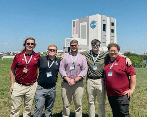 Group of students posing for a photo with the NASA building in the background