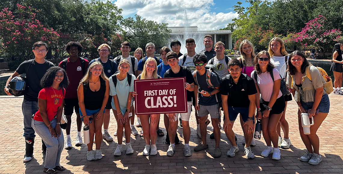 Kamryn Carter with a group of other students holding up a sign that reads, "First day of class!"