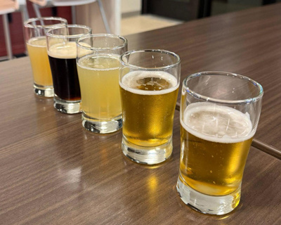 A close up of five glasses with each containing amber-colored liquids in varying shades.