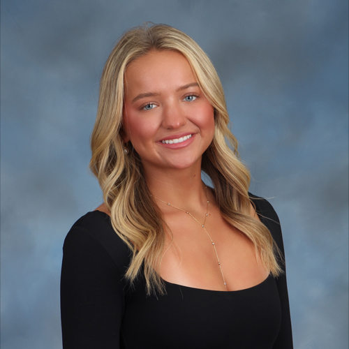 Blonde woman in front of a gray-blue background, wearing a black blouse.