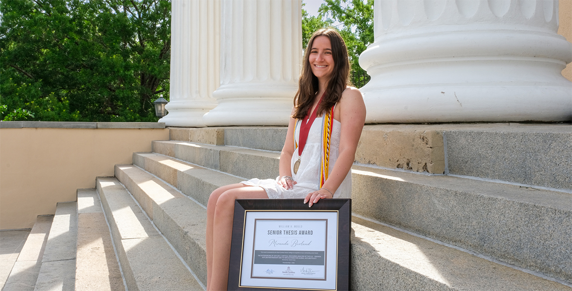 Miranda Borland posing for her graduation photos with her framed senior thesis award.