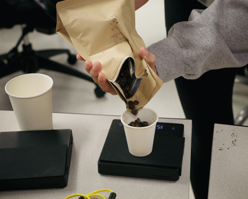 A student pouring coffee beans into a cup.