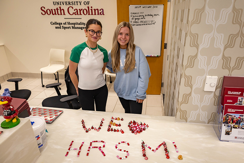 Two HRSM students pose for a photo behind the desk at the Welcome Center on Valentine's Day with the words "We Love HRSM!" spelled out on the table with candy.